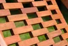 A close-up view of a wooden slatted surface, likely part of outdoor furniture, with a blurred green background. Podgląd zdjęcia produktu