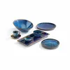 A collection of blue ceramic tableware, including bowls, cups, and plates, arranged on a white background. Produktbild-Vorschau