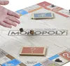 A hand is shown throwing dice on a Monopoly board, with cards and game pieces visible. Produktbild-Vorschau