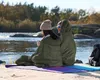 Two people sitting by a river, wrapped in sleeping bags. Náhľad obrázku produktu