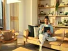 A man is sitting on a couch using a tablet in a well-lit living room. Produktbild-Vorschau
