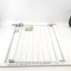 A white metal baby gate is laid out on a white background, with some accessories scattered nearby. Produktbild-Vorschau