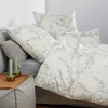 A bed with pillows and a duvet featuring a floral pattern, with candles on a tray in the foreground. Produktbild-Vorschau