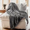 A plush gray blanket draped over a white sofa with a textured pillow. Produktbild-Vorschau