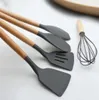 A set of kitchen utensils with wooden handles and gray silicone heads, including spatulas and a whisk, laid out on a white surface. Náhľad obrázku produktu