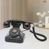 A black retro rotary dial telephone is placed on a white desk. Podgląd zdjęcia produktu