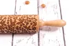 A wooden rolling pin with an engraved floral pattern rests on a white wooden surface. Produktbild-Vorschau