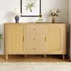 A modern wooden sideboard with rattan doors and gold handles, displayed in a well-lit room with a painting and a vase of flowers on top. Voir les images du produit