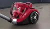 A red vacuum cleaner is shown on a floor with a black cord extending into the background. Voir les images du produit