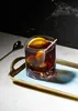 A cocktail with an orange slice and olives on a tray, with a spoon and a marble background. Produktbild-Vorschau