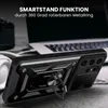 A black phone case with a ring stand is displayed on a surface, with a laptop and headphones in the background. Produktbild-Vorschau