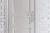 A close-up view of a white door with a silver door handle, next to a white brick wall with an electrical outlet. Anteprima dell’immagine prodotto