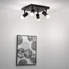 A black ceiling light fixture with four adjustable spotlights is mounted on a white ceiling. Below the light fixture, a framed piece of abstract art with circular patterns hangs on a white wall. Voir les images du produit
