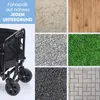 A collage showing a black foldable wagon with small wheels, alongside various ground textures like dirt, gravel, grass, wood, and pavement. Podgląd zdjęcia produktu