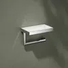 A chrome and glass toilet paper holder with a shelf mounted on a gray wall. Produktbild-Vorschau