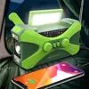 An emergency radio with a built-in flashlight and LED panel is placed on a green surface, with a smartphone in the foreground. Produktbild-Vorschau