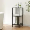 A black metal shelving unit with three shelves, placed next to a white bathtub in a bathroom. The shelves hold towels, soap, and lotion dispensers. There are also decorative candles and a small plant on the top shelf. Produktbild-Vorschau