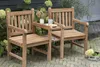 Two wooden chairs with a small table between them, set on a brick patio with plants in the background. Produktbild-Vorschau