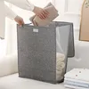 A person is placing folded towels into a gray laundry basket. Produktbild-Vorschau