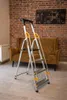 A step ladder is placed in front of a sofa in a room with a brick wall. Anteprima dell’immagine prodotto
