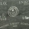 A close-up view of a textured gray fabric with white text and graphics printed on it, likely a home decor item. Produktbild-Vorschau