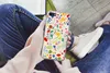 A person is holding a phone with a floral pattern case while sitting down. Produktbild-Vorschau