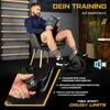 A man is sitting on a chair and reading a book while using a mini bike pedal trainer. Produktbild-Vorschau