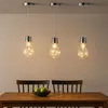 Three pendant lights with Edison-style bulbs hanging over a wooden dining table. Produktbild-Vorschau