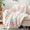 A fluffy, rainbow-colored blanket draped over a sofa, with icons indicating its features. Produktbild-Vorschau