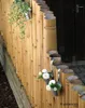 A fence made of bamboo poles with hanging planters containing green foliage and white flowers. Voir les images du produit
