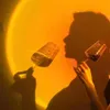 Two people holding wine glasses in front of a sunset lamp. Produktbild-Vorschau