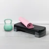 A kettlebell, a yoga mat, and a step platform are arranged on a light-colored floor against a white wall. Náhled obrázku produktu
