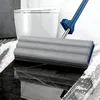 Grauer Flachwischer mit blauem Griff reinigt einen schwarzen Marmorboden mit Seifenschaum, im Hintergrund eine weiße Toilette Anteprima dell’immagine prodotto