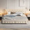 A bedroom scene featuring a tufted beige bed with storage drawers, dressed with pillows and a throw blanket. Produktbild-Vorschau
