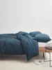 A bed with indigo blue linen bedding and pillows, with a small chair and a book with a cup of coffee on the floor. Produktbild-Vorschau