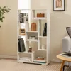 A white geometric bookshelf filled with books and decorative items, placed in a room with a light-colored rug and a hint of a sofa and coffee table. Podgląd zdjęcia produktu
