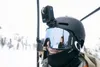 A person wearing a ski helmet with a GoPro camera attached, riding a ski lift in a snowy mountain environment. Produktbild-Vorschau