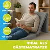 A man is reading a book while sitting on a folded mattress in a living room. Produktbild-Vorschau