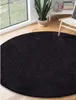 A black round rug is placed on a wooden floor next to a large window. A potted plant and a chair are visible in the background. Produktbild-Vorschau