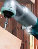 A close-up shot of a cordless angle impact wrench driving a screw into a piece of wood, with wooden framing in the background. Náhled obrázku produktu