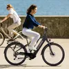 Two women riding e-bikes along a waterfront promenade. Produktbild-Vorschau