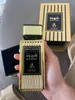 A hand holding a gold and black perfume bottle with its box in the background. Produktbild-Vorschau