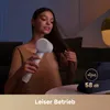 A woman is drying her hair with a white hairdryer in a dimly lit room, with a tablet displaying sound waves and decibel level on a table in the foreground. Produktbild-Vorschau