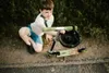 A young boy is kneeling next to a scooter, holding a helmet. Produktbild-Vorschau
