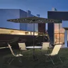 An outdoor patio set with a table, chairs, and an umbrella with LED lights at dusk. Produktbild-Vorschau