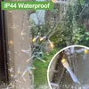 A string of fairy lights with yellow LEDs, seen through a window with water droplets on it. The lights are white and clear. Produktbild-Vorschau