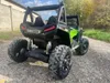 Rear view of a green and black children's electric UTV parked on a gravel path with trees and a building in the background. Produktbild-Vorschau