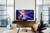 A modern living room with a large TV displaying a colorful abstract image, a comfortable armchair with a blanket, and decorative shelving. Produktbild-Vorschau