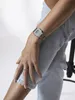 A close-up shot of a person's arm and leg wearing a watch and jeans. Produktbild-Vorschau