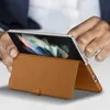 A person's hands are holding a folded smartphone with a brown leather case, which is propped up as a stand. Produktbild-Vorschau